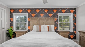 Une chambre à coucher avec un grand lit, deux tables de chevet, une tête de lit en bois et une fenêtre donnant sur des arbres.