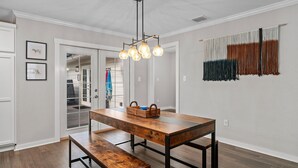 Un coin repas avec une table et un banc en bois, un luminaire suspendu et une vue sur un placard où sont accrochés des vêtements.