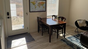 Un comedor con una mesa de madera, cuatro sillas, un mapa mundial en la pared y vistas a través de una puerta.