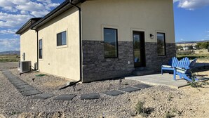 Un pequeño edificio de una sola planta con fachada color beige y detalles de piedra, que presenta una puerta y ventanas, y una silla Adirondack azul en el exterior.