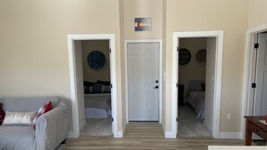 Un salón espacioso con un sofá, una puerta que da a un dormitorio y un pasillo con otra puerta al final.