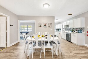 A modern kitchen with white cabinetry, a dining area with a round table and chairs, and a visible entrance door.