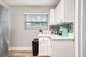A kitchen with white cabinets, a coffee bar, a toaster, a blender, and a trash bin.