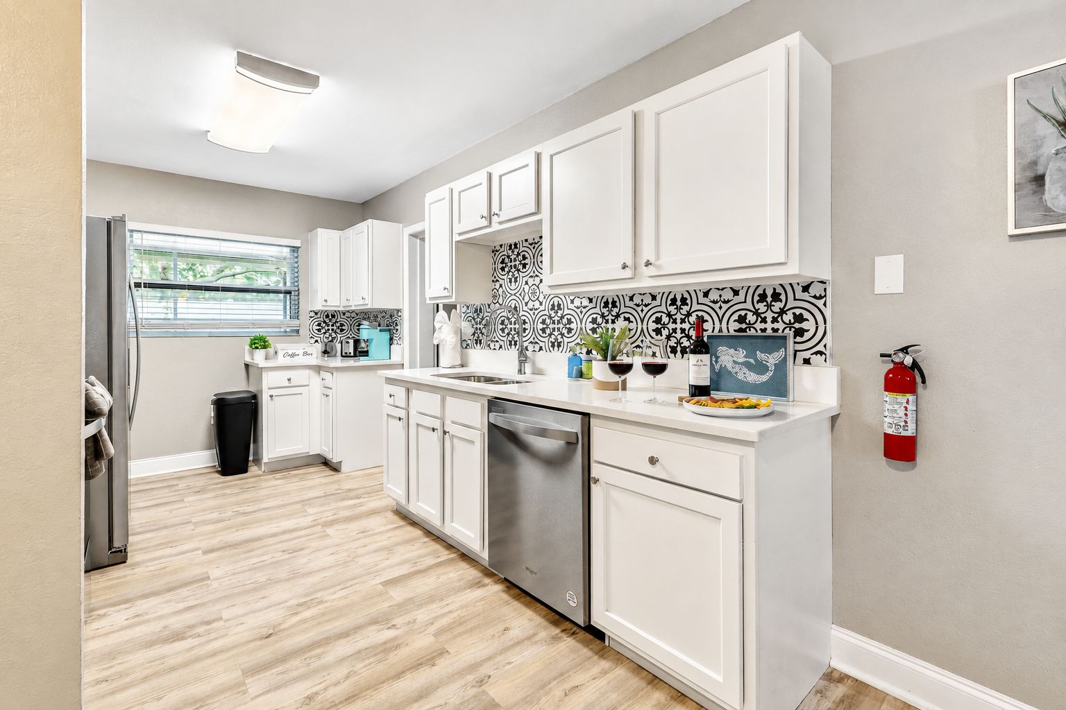 A modern kitchen with white cabinetry, a stainless steel dishwasher, and a black and white patterned backsplash.