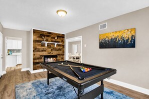Uma mesa de bilhar em um espaço com lareira, área de refeições e um quadro na parede.