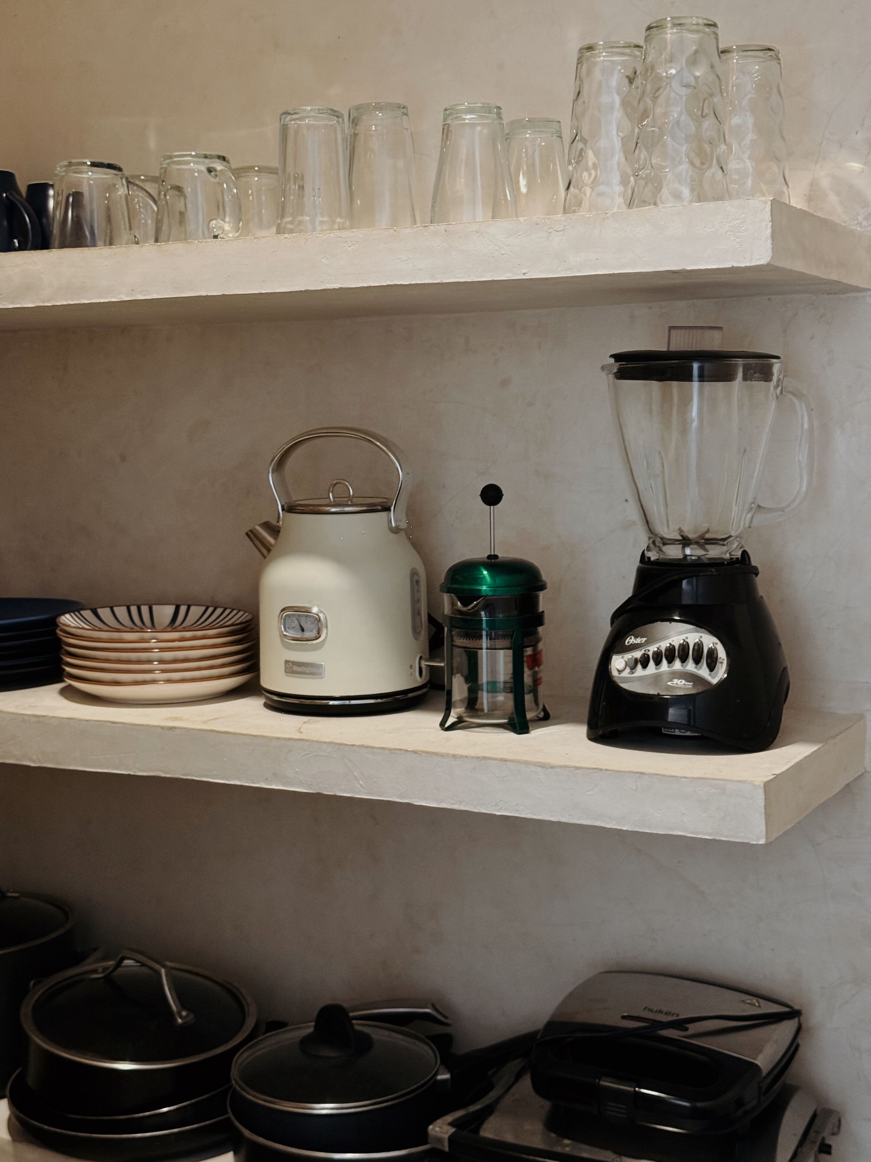 Uma prateleira na cozinha com uma chaleira, um liquidificador e vários potes de vidro.