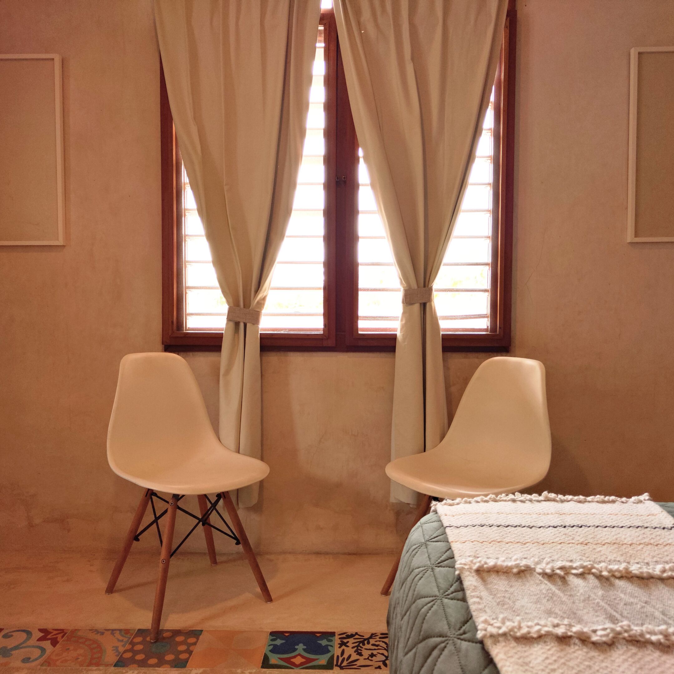 A room with two white chairs, a bed with a quilt, and a window with curtains.