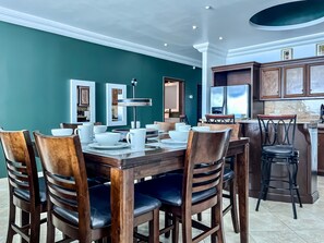 Un coin repas avec une table et des chaises en bois, une cuisine à l’arrière-plan et des murs de couleur turquoise.