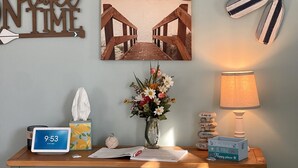 En vägg med en strandmotiv, träbokstäver som stavar ordet ”RELAX BEACH”, en klocka, en vas med blommor och en lampa.