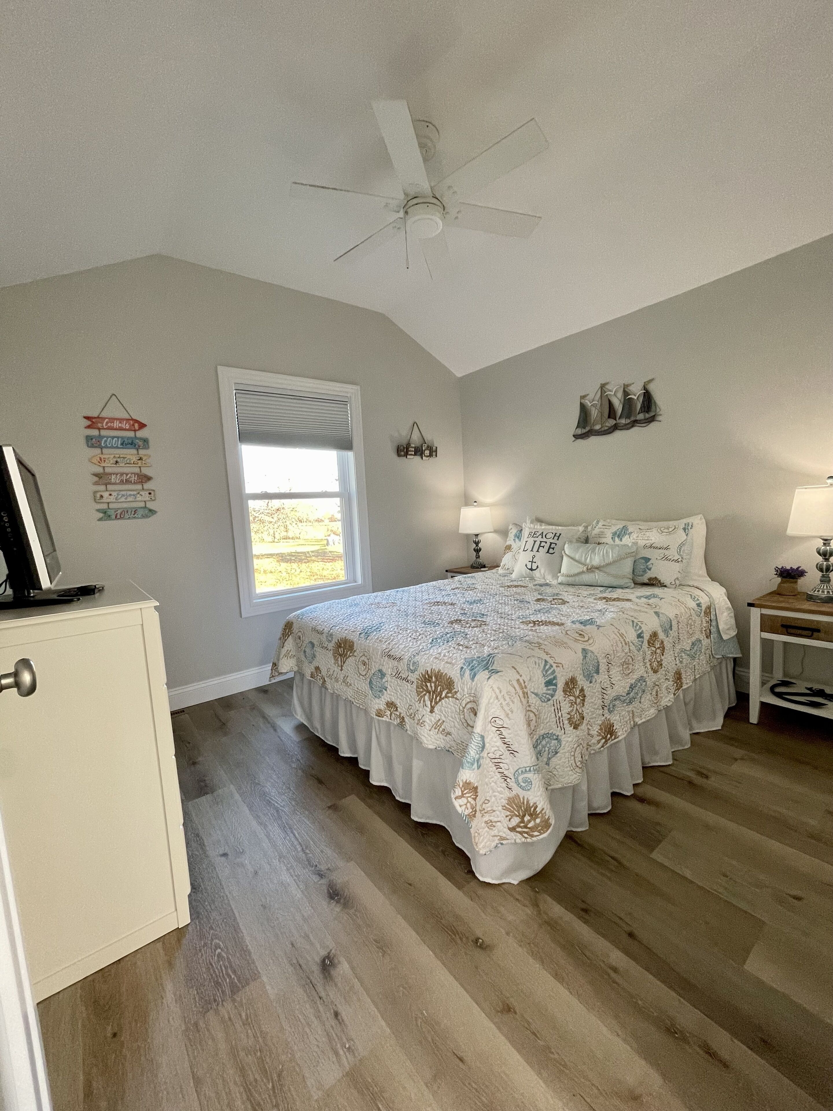 A bedroom with a bed, a ceiling fan, a window, a nightstand, and a dresser.