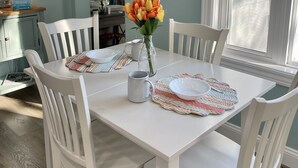 En matplats med ett vitt bord dukat för fyra personer, omgivet av vita stolar. En vas med blommor står på bordet, och det finns bordsdekorationer på bordet.