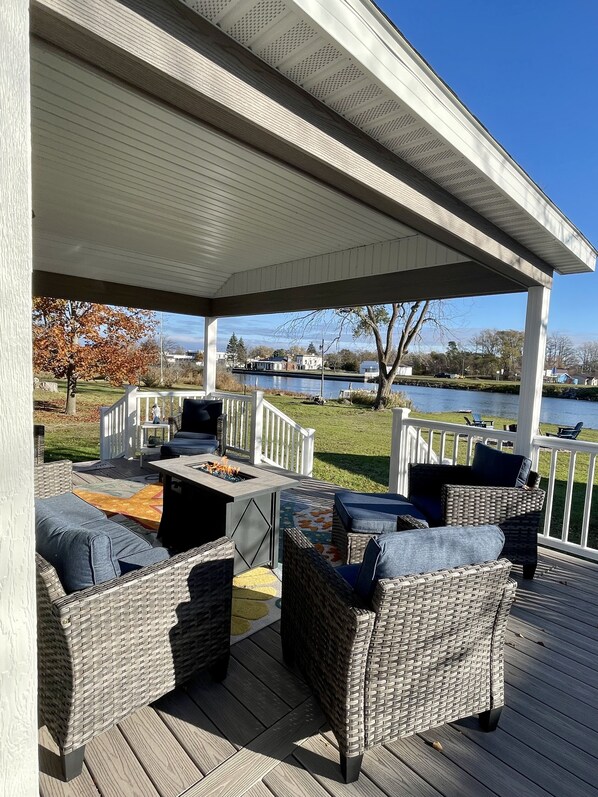 A covered outdoor deck with wicker furniture, a fire pit, and a view of a lake.