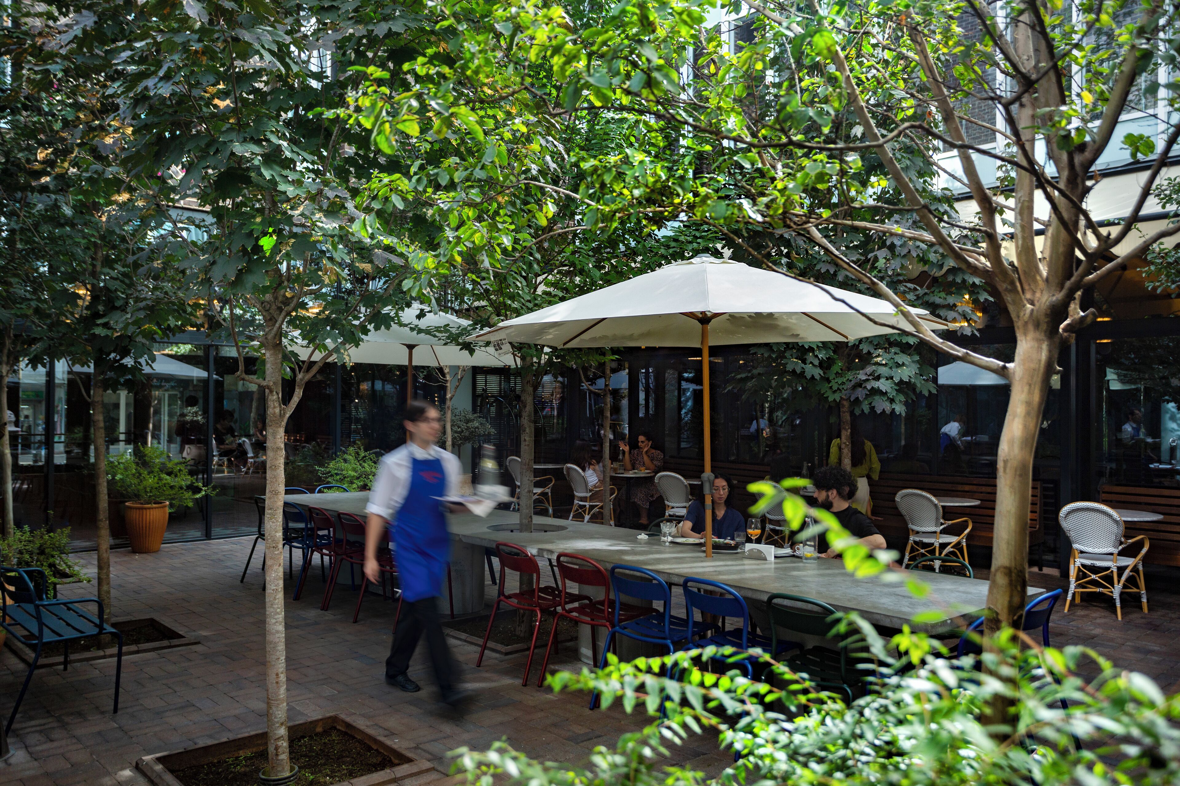 An outdoor dining area with tables and chairs, surrounded by trees and potted plants.