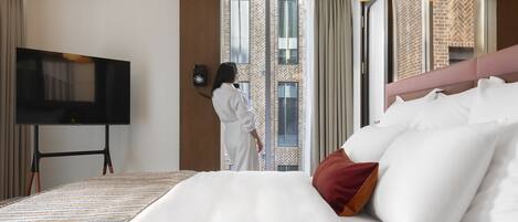 Habitación de hotel con una cama grande, un televisor y vista a un edificio por la ventana.