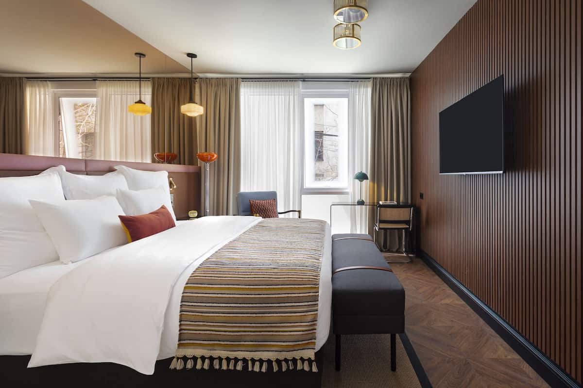 A hotel room with a large bed, a desk, a television, and a window with curtains.