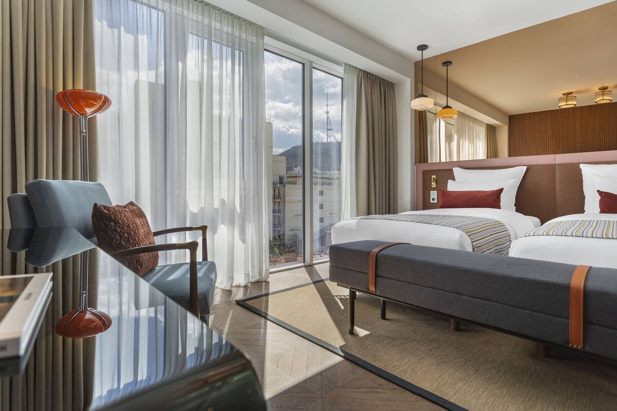 A hotel room with a large bed, a sofa, a desk, and a view of the city.