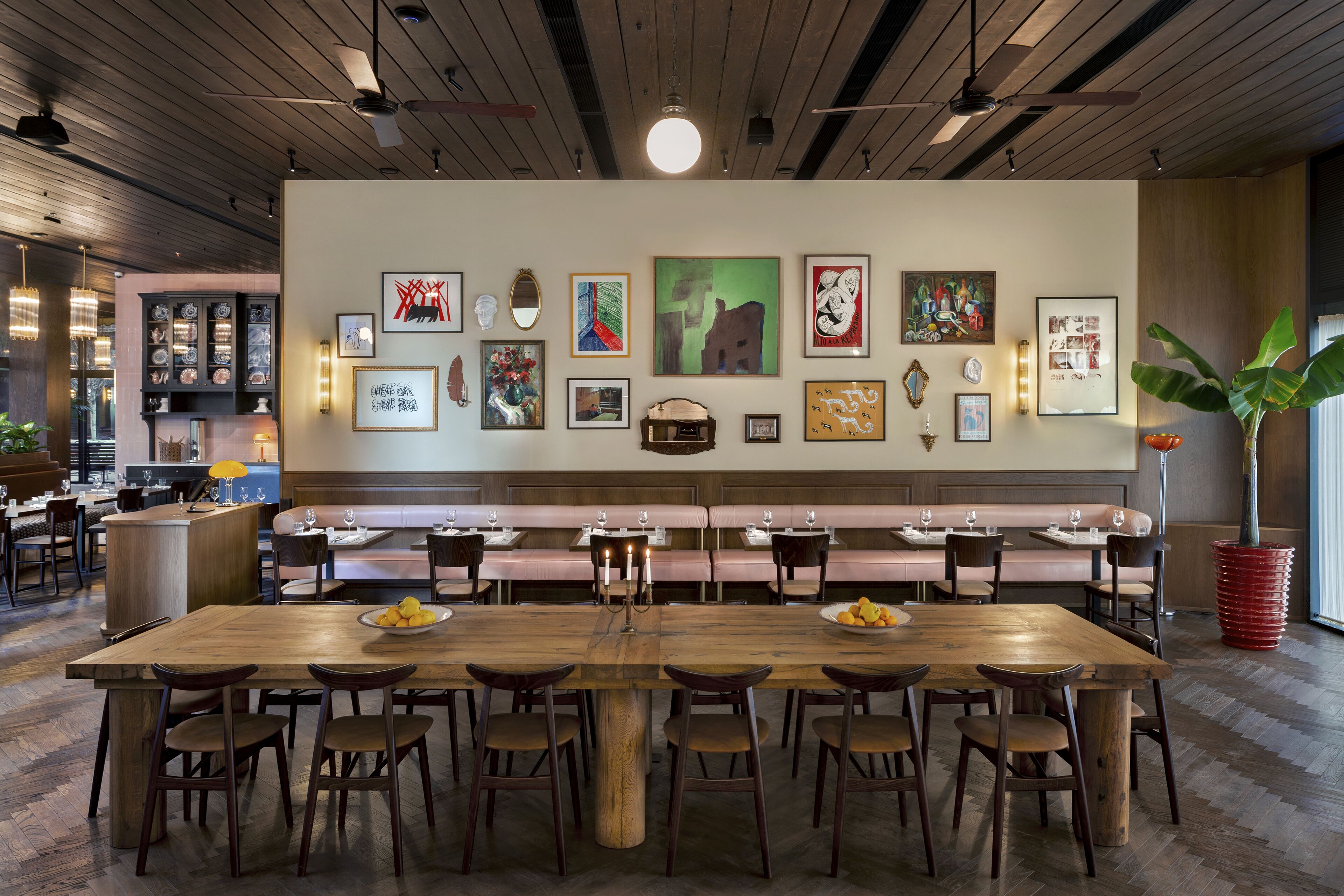 A restaurant with a long wooden table, multiple seating options, and a wall adorned with various framed artworks.