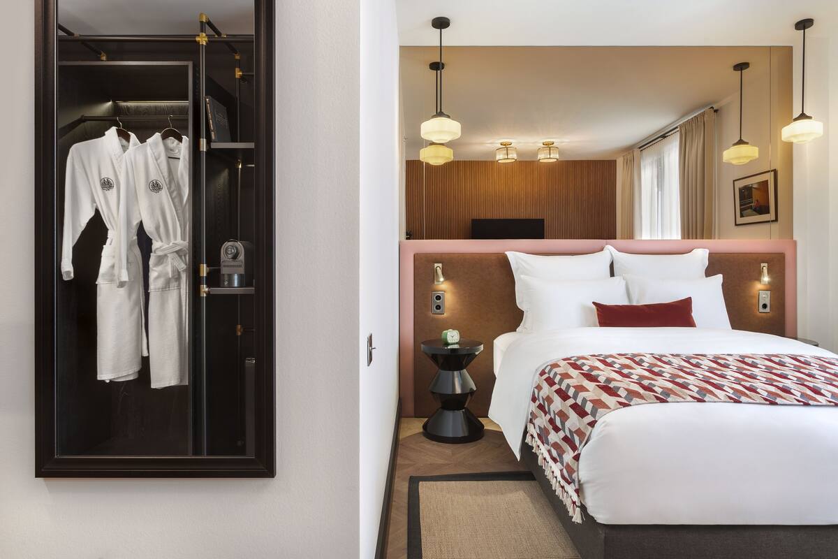 A hotel room with a bed, bedside table, and a wardrobe with hanging robes.
