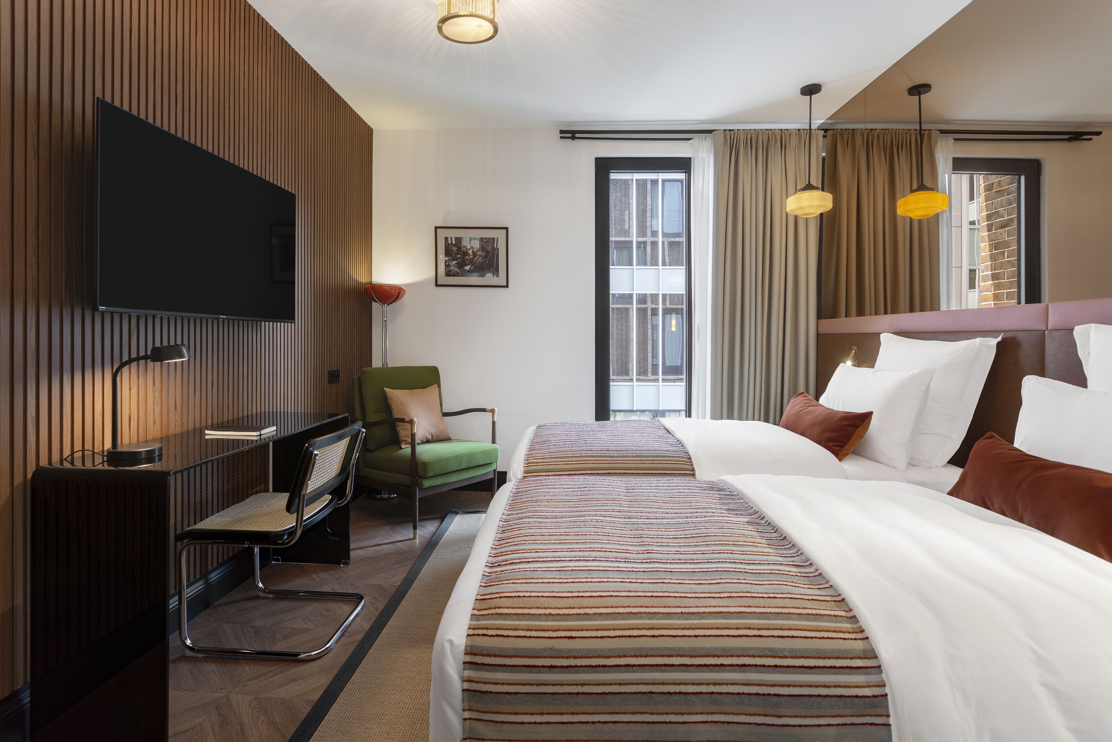 Una habitación de hotel con cama, escritorio, silla, televisor y ventana con cortinas.