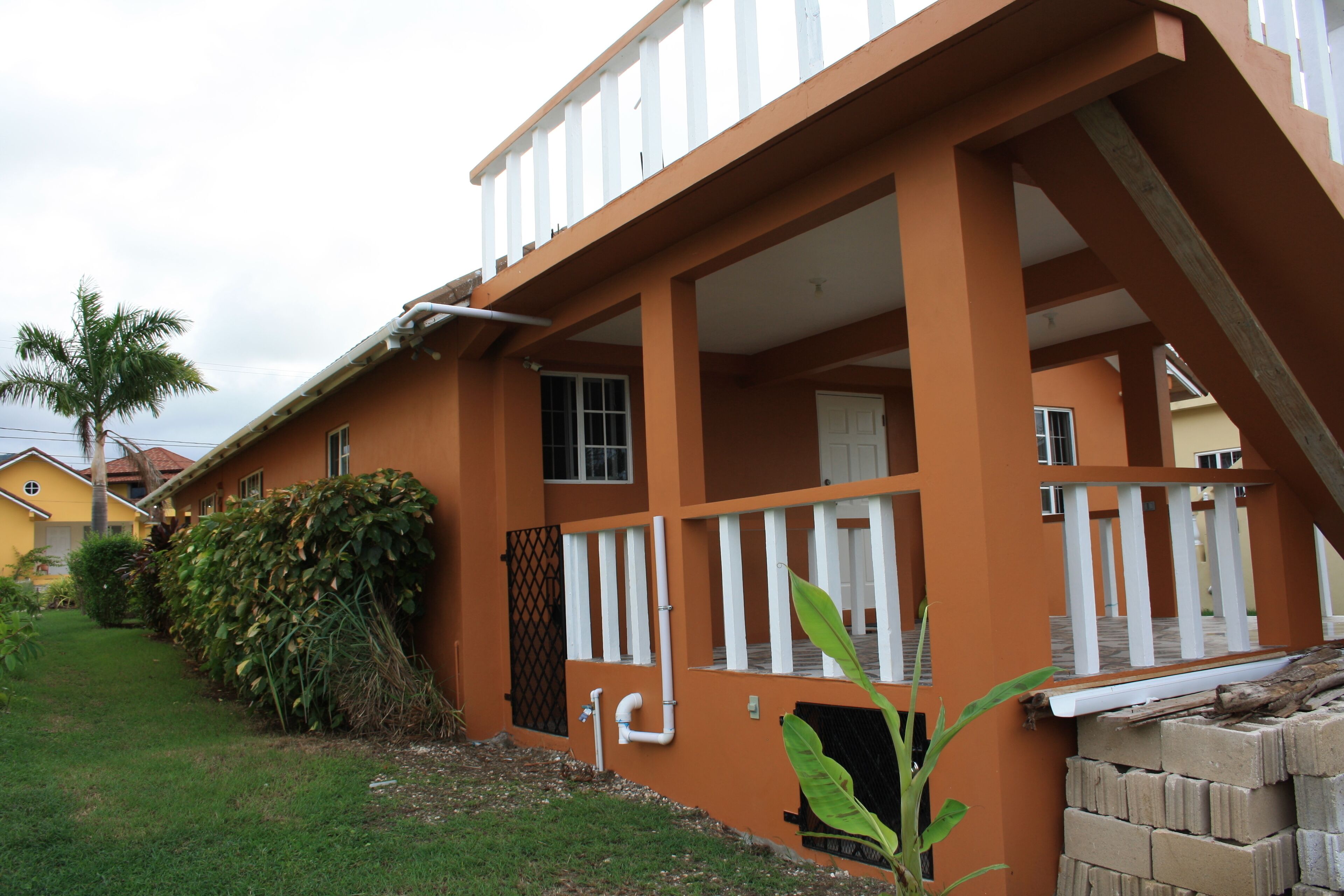 A two-story building with a balcony, a small garden, and a brick structure.