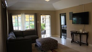 A living room with a sofa, ottoman, and a television on a stand. - Soleil Hartland Palms (St. Ann's Bay)