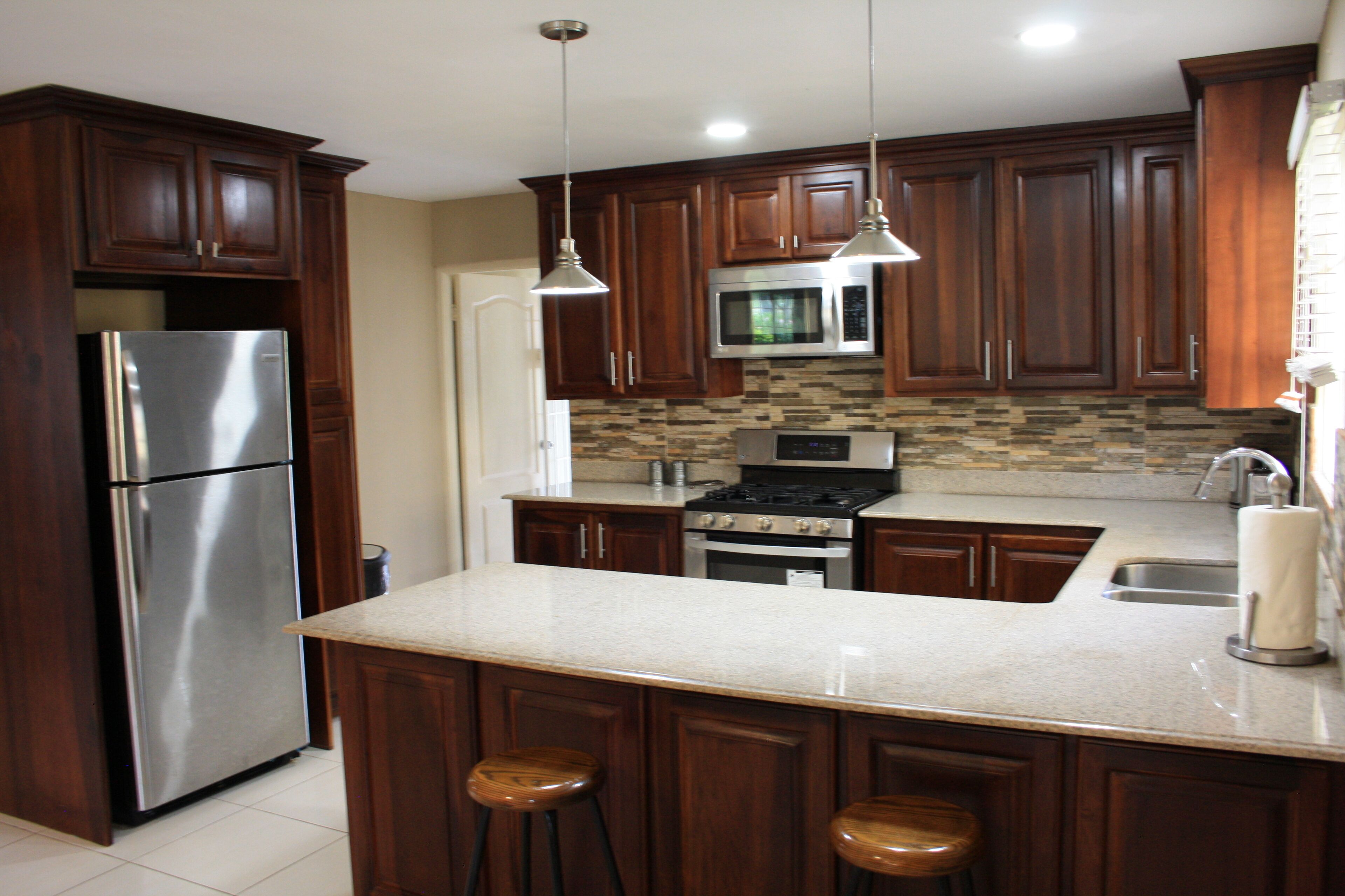 Una cocina con armarios de madera, electrodomésticos de acero inoxidable, encimera de granito e iluminación colgante.