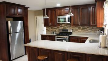 Una cocina con armarios de madera, electrodomésticos de acero inoxidable, encimera de granito e iluminación colgante.