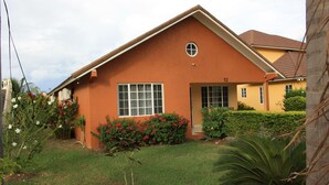 A single-story house with a brown exterior, a front door, and a small circular window above the door. - Soleil Hartland Palms (St. Ann's Bay)