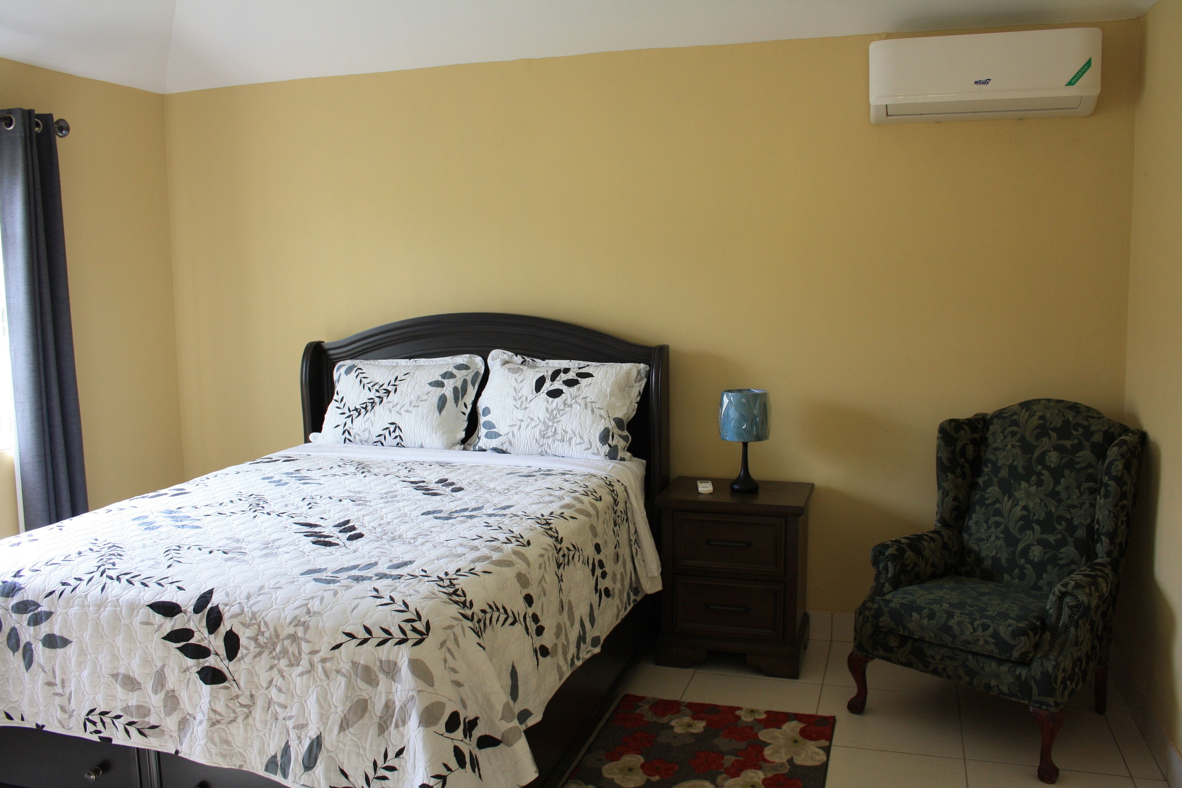 A bedroom with a bed, a chair, a nightstand, and an air conditioner.