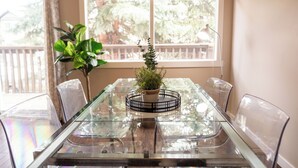 A glass-top dining table with chairs, a potted plant, and a view of a balcony with a railing. - Near Riverside Sunset-Lodge w/Backyard+BathTub-W/D (Calgary)