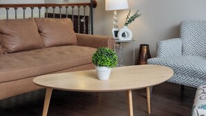 A living room with a brown sofa, a round wooden coffee table with a potted plant, a patterned armchair, and a small side table with a lamp and decorative items. - Near Riverside Sunset-Lodge w/Backyard+BathTub-W/D (Calgary)