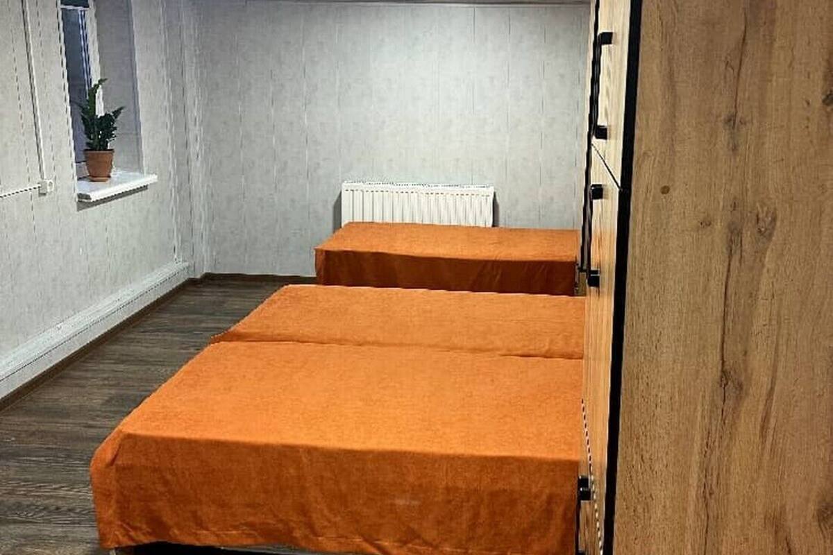 A room with two beds, a radiator, a window with a plant, and a wooden wardrobe.