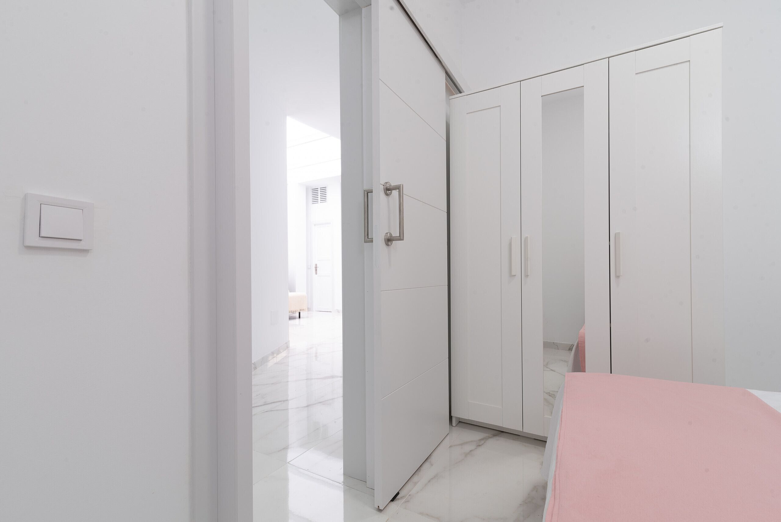 A modern, minimalist room with a white wardrobe, a marble floor, and a visible light switch.