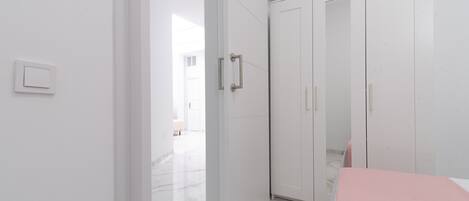 A modern, minimalist room with a white wardrobe, a marble floor, and a visible light switch.