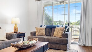 A living room with a sofa, a coffee table with a basket, a lamp, and a view of the outdoors through large windows.