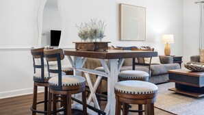 A dining area with a wooden table and chairs, a vase with flowers, and a sofa in the background.