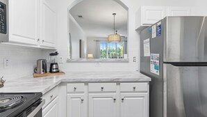 A modern kitchen with white cabinets, a stainless steel refrigerator, a built-in oven, and a coffee maker.