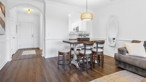 A modern kitchen with white cabinets, a wooden dining table, and bar stools.