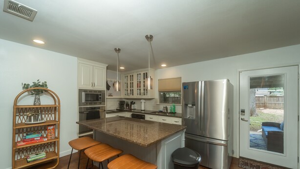 A modern kitchen with a central island, stainless steel appliances, and a built-in oven. - Stylish Group Retreat • Hot Tub • Game Room • Yard (Austin)