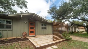 A residential house with a front porch, a wooden gate, and a well-maintained lawn. - Stylish Group Retreat • Hot Tub • Game Room • Yard (Austin)