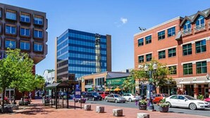 A street view with a modern building, a plaza with benches, and a restaurant. - Studio 5~ Cozy BDRM w/ Private Bath (Moncton)