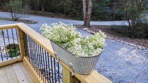 Ein Metallpflanzgefäß mit weißen Blüten auf einer Holzdeckengeländer.
