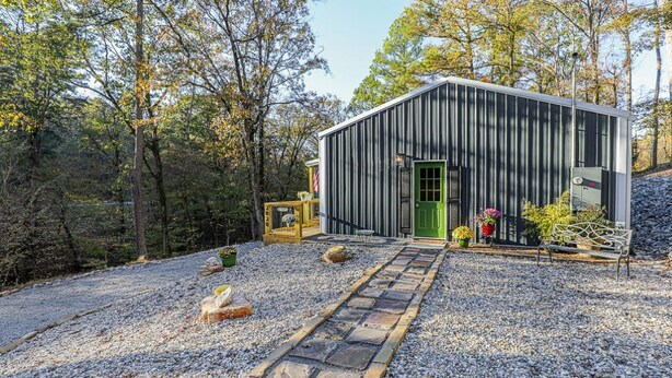 Eine rustikale Holzhütte mit grüner Tür, umgeben von Kies und Bäumen.