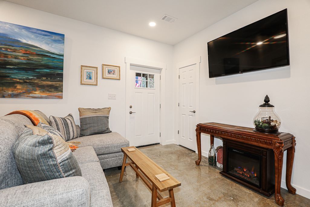 A living room with a grey sofa, a wooden bench, a fireplace, and a flat-screen TV mounted on the wall.