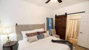 Ein Schlafzimmer mit einem Bett, einem Nachttisch, einer Lampe, einem Holzschrank und einer Tür zu einem anderen Raum.