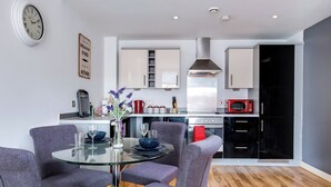 A modern kitchen with a dining area, featuring a glass table, grey upholstered chairs, and a variety of appliances including a microwave and stove. - From Home to Home (Birmingham)