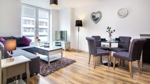 A modern living room with a sofa, a dining table with chairs, a lamp, and a TV. - From Home to Home (Birmingham)
