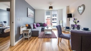 A modern living room with a grey sofa, a white coffee table, and a dining area with a glass table and purple chairs. - From Home to Home (Birmingham)