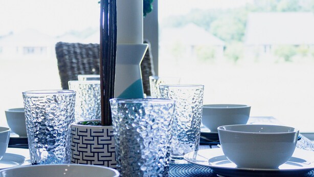 A dining table set with clear glassware, white bowls, and a decorative blue plant. - Charming Brand New Home in Foley (Foley)