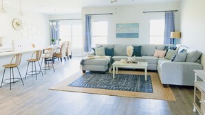A spacious living room with a grey sofa, a coffee table, and a dining area with chairs and a table. - Charming Brand New Home in Foley (Foley)
